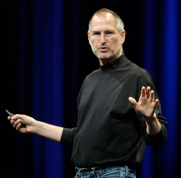 Steve Jobs vorbind pe scenă, cu o mână ridicată